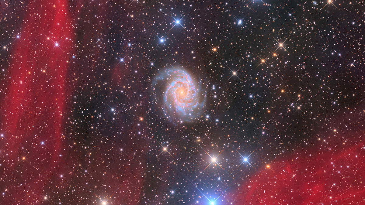 Spiral galaxy surrounded by colorful stars and red nebulae captured in breathtaking space photos from astronomy photography.
