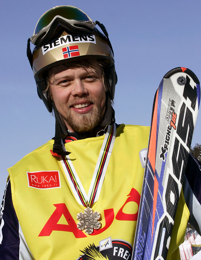 Olympic medalist skier smiling with helmet and ski gear after winning a competition outdoors on a clear day Olympic medalist skier smiling with helmet and ski gear after winning a competition outdoors on a clear day