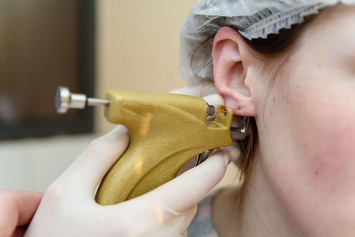 Close-up of unlicensed ear piercing with a gold stud being inserted into a woman’s ear during a baby visit. Close-up of unlicensed ear piercing with a gold stud being inserted into a woman’s ear during a baby visit.