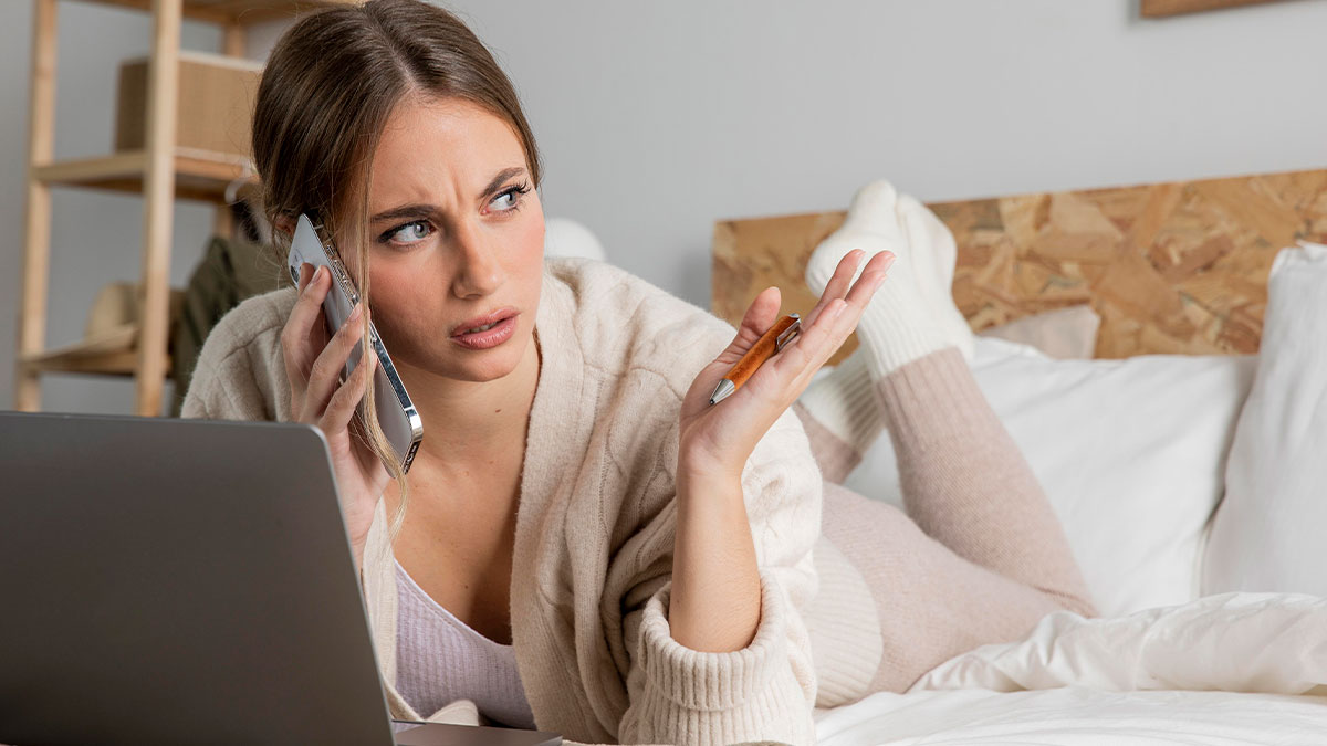 Woman lying on bed talking on phone with frustrated expression, dealing with couple's childfree sis babysitting request.