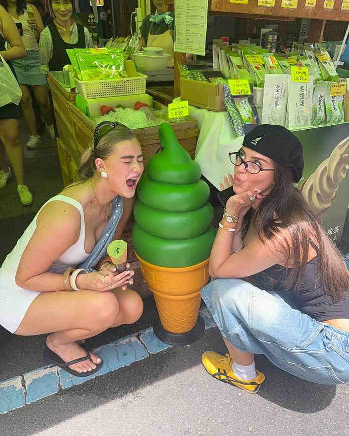 Two young women posing with a large green ice cream cone outside a market during an Australian influencer Japan trip. Two young women posing with a large green ice cream cone outside a market during an Australian influencer Japan trip.