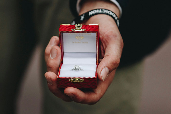 Hand holding an open red ring box with a diamond engagement ring, related to man public proposal at wedding story.
