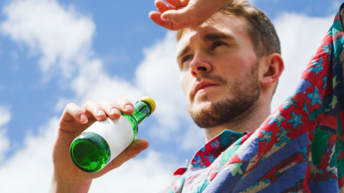 Man shielding eyes from sun holding green bottle outdoors warning about extreme heat alcohol risks in 18 states