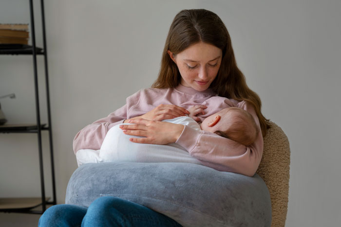 Mother cradling infant closely while seated, showing tender moment between parent and baby indoors. Mother cradling infant closely while seated, showing tender moment between parent and baby indoors.