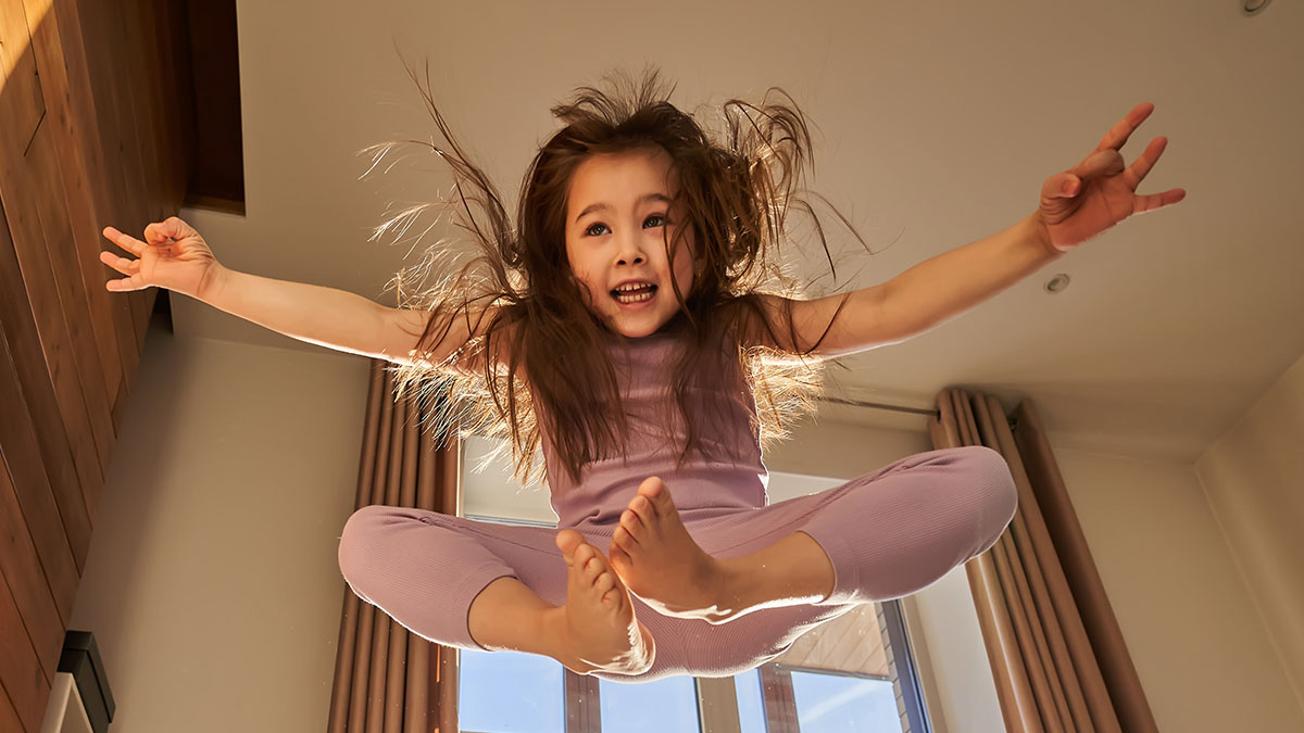 Energetic 6-year-old girl jumping indoors with a wild hair sugar rush, embodying mini metalhead excitement during babysitting.