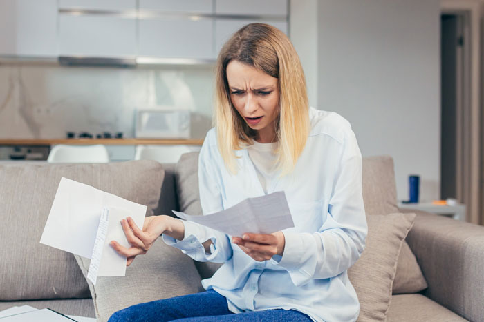 Woman looking confused while holding papers on a couch, babysit newphews study Bible concept in a home setting Woman looking confused while holding papers on a couch, babysit newphews study Bible concept in a home setting
