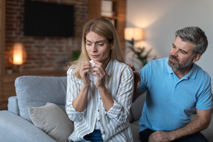 Woman upset on couch holding tissue while man comforts her during a tense family discussion about babysitting step-siblings. Woman upset on couch holding tissue while man comforts her during a tense family discussion about babysitting step-siblings.