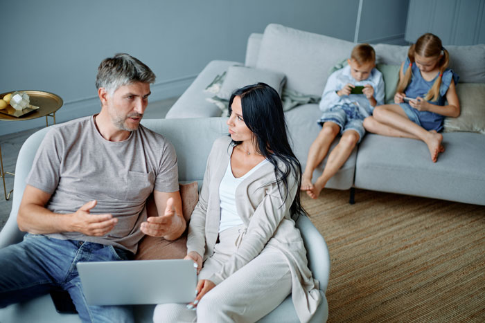 Parents having a serious discussion on couch while two children ignore them, illustrating babysitting step-siblings challenge. Parents having a serious discussion on couch while two children ignore them, illustrating babysitting step-siblings challenge.