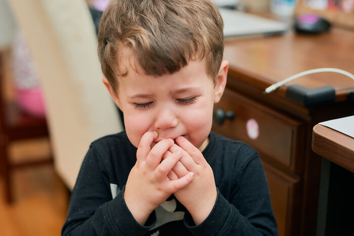 Young boy crying indoors with hands near his mouth, illustrating creepy babysitter stories that send a shiver down your spine.