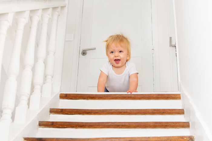Toddler crawling up wooden stairs inside a white home, illustrating a scene for creepy babysitter stories keyword.