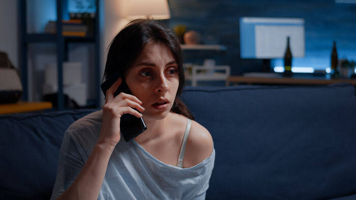 Worried babysitter talking on the phone at night in a dimly lit living room, capturing creepy babysitter stories mood.