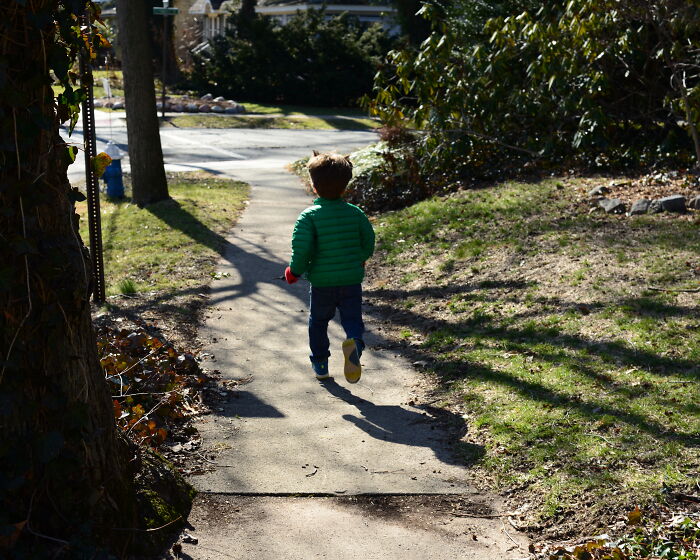 Child walking alone on a suburban sidewalk in a green jacket, evoking creepy babysitter stories and eerie moments outdoors.