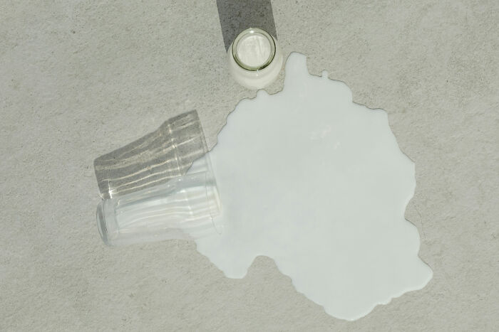 Spilled milk with empty glass and baby bottle shadow on floor, evoking creepy stories from babysitters atmosphere.