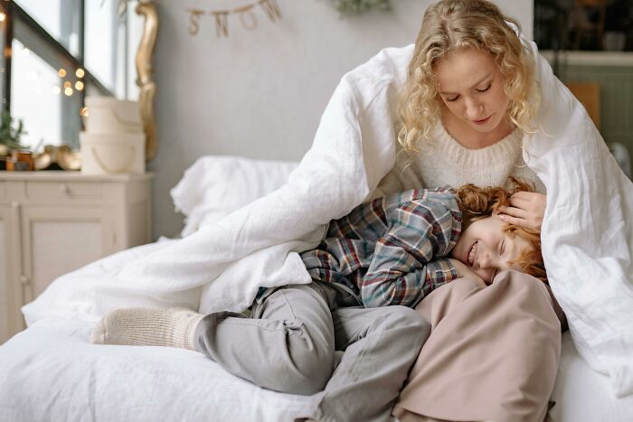 Babysitter comforting a child wrapped in a white blanket on a cozy bed, evoking creepy babysitter stories atmosphere.