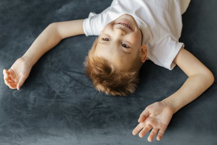 Smiling young boy lying on dark carpet playing indoors, related to creepy babysitter stories and chilling experiences.