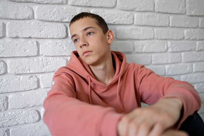 Teen boy in a pink hoodie looking pensive, reflecting on expectations as an absentee mom depends on him for babysitting. Teen boy in a pink hoodie looking pensive, reflecting on expectations as an absentee mom depends on him for babysitting.