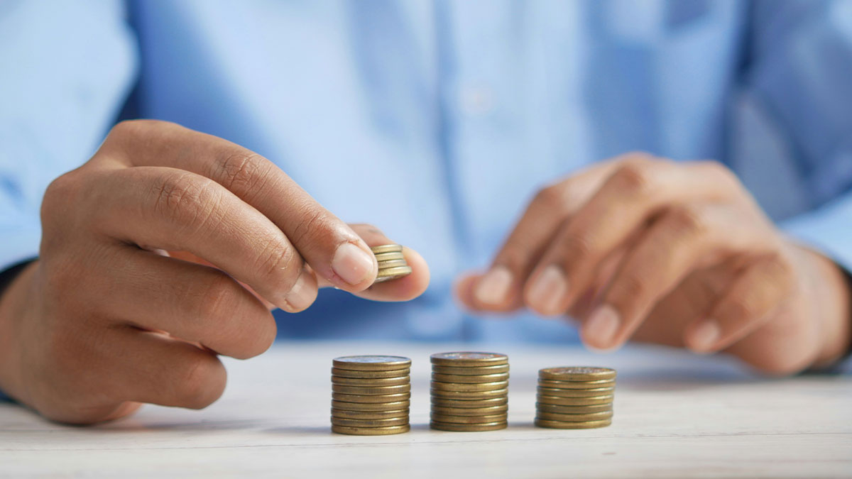 Person stacking coins on a table, demonstrating basic skills related to money management and organization.