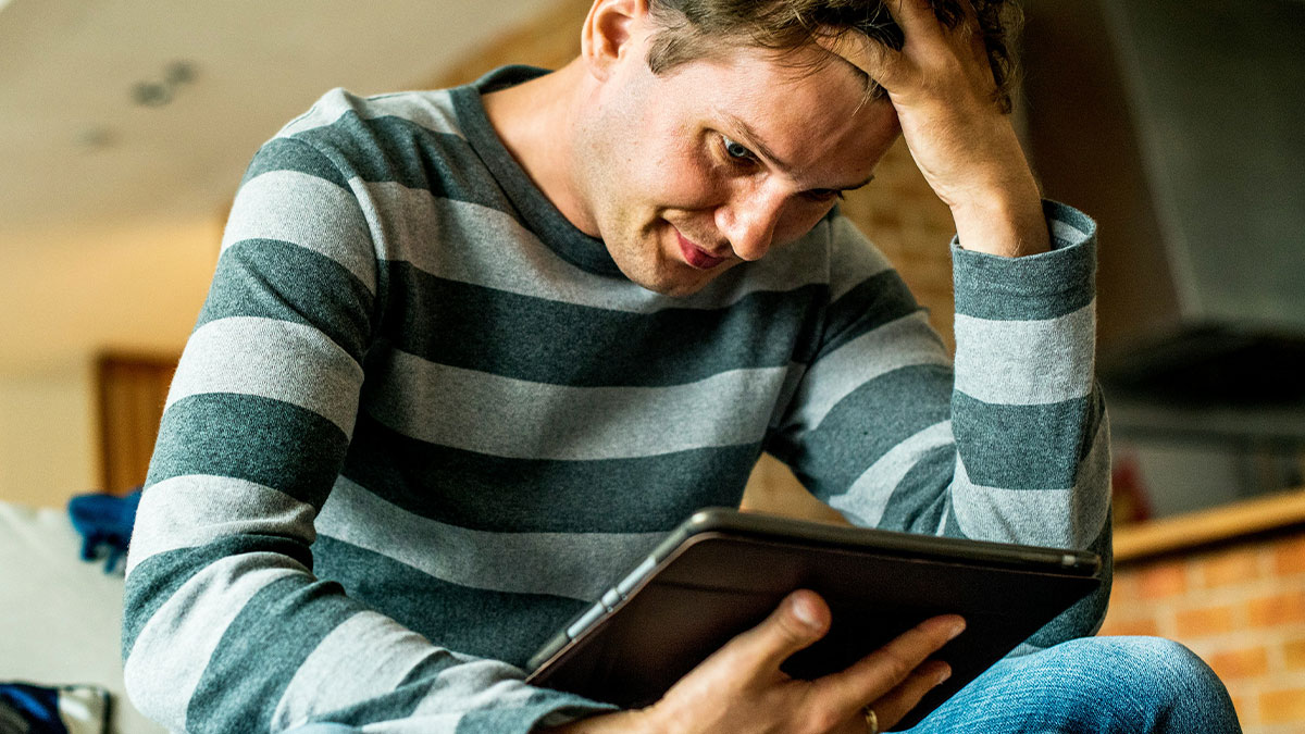 Man in striped shirt looking stressed while using a tablet, relating to best friend and girlfriend situation checking email