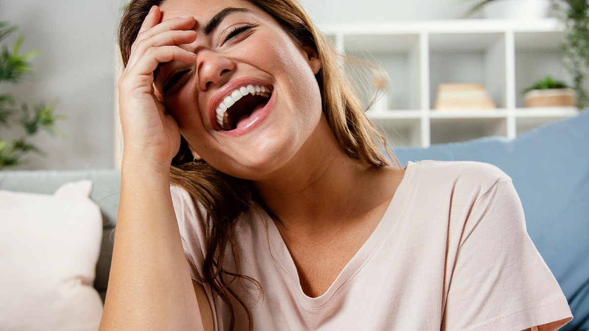 Woman laughing joyfully at home, capturing the spirit of hilariously relatable friendship memes.