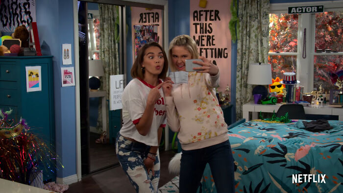 Two young women taking a selfie in a colorful bedroom from a popular Netflix show that keeps viewers coming back for more
