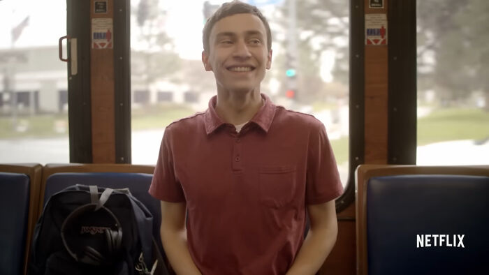 Young man smiling on a bus, with backpack and headphones, scene from one of the best Netflix shows keeping viewers coming back