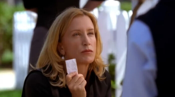 Woman with blonde hair holding a small white packet, watching intently in a scene from popular Netflix shows.