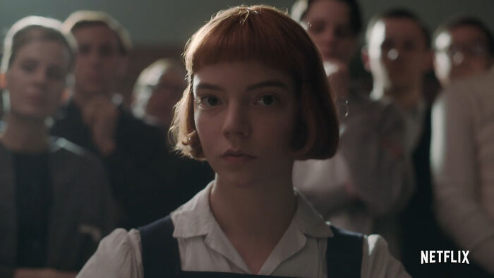 Young woman with short hair in a school uniform surrounded by others, representing popular Netflix shows fans keep returning to.