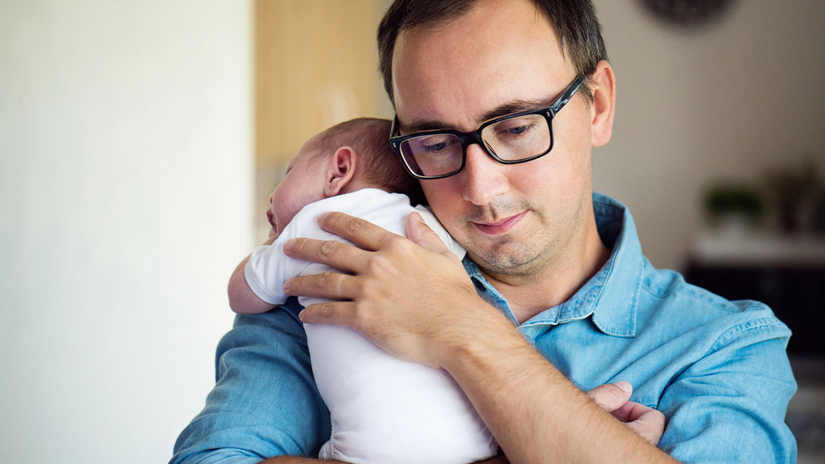 Man with glasses gently holding a newborn baby, reflecting bio dad family drama and babysit refusal issues at home.
