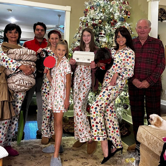 Family in colorful pajamas gathered by a decorated Christmas tree, representing sisters lost in Texas floods with hands locked together. Family in colorful pajamas gathered by a decorated Christmas tree, representing sisters lost in Texas floods with hands locked together.