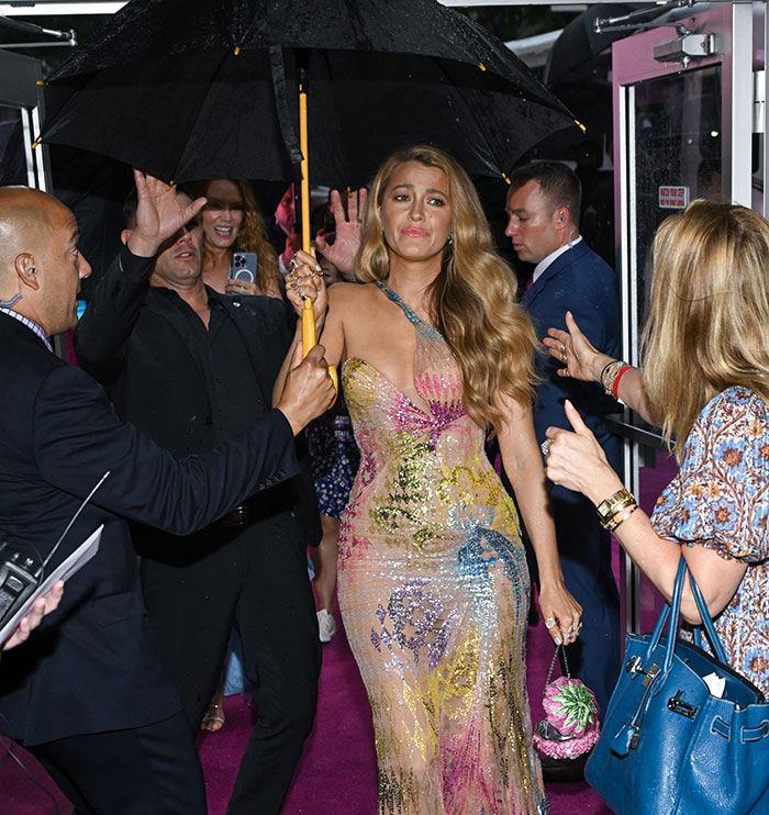 Blake Lively attending event in glamorous dress as security holds umbrella on a rainy night. Blake Lively attending event in glamorous dress as security holds umbrella on a rainy night.
