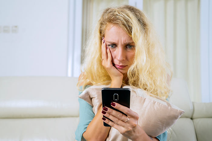 Single mom looking uncomfortable at phone while sitting on couch, feeling uneasy about her boss contacting her at home. Single mom looking uncomfortable at phone while sitting on couch, feeling uneasy about her boss contacting her at home.