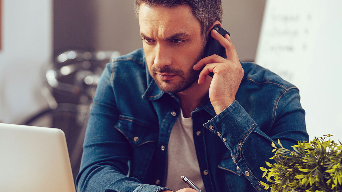 Man in denim jacket messaging after every client on phone, looking focused and waiting for a response in office.