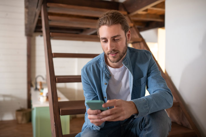 Young man sitting on wooden stairs holding a phone, representing a boyfriend who breaks up without warning and blocks contact.