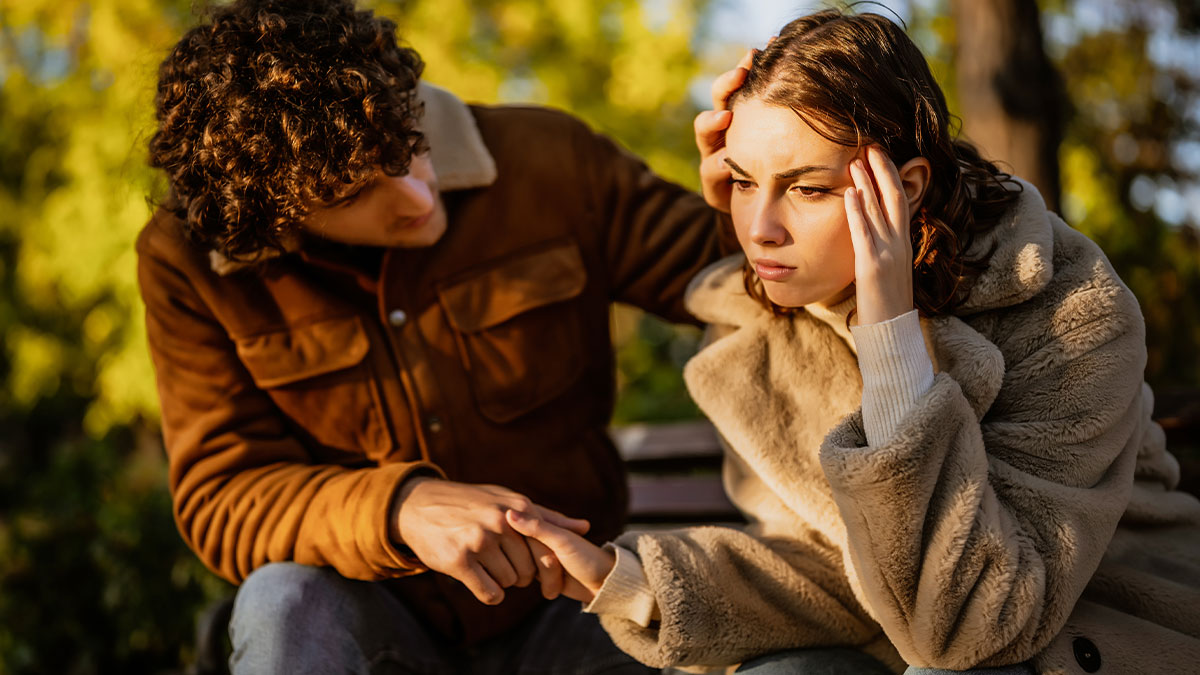 Couple sitting outside, man comforting upset woman who looks frustrated, illustrating relationship breakup and blocked contact.