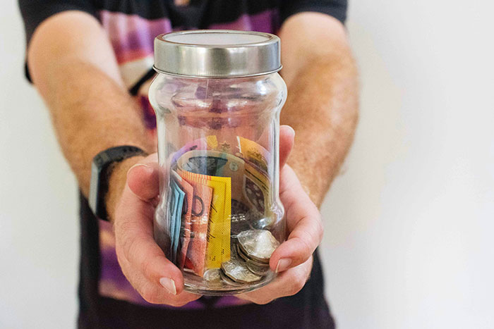 Man holding a jar filled with coins and bills, symbolizing funds for a cycle trip instead of watching his daughter. Man holding a jar filled with coins and bills, symbolizing funds for a cycle trip instead of watching his daughter.