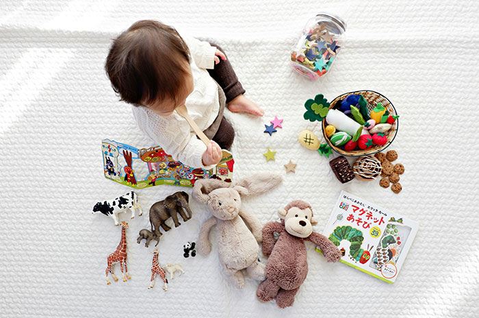 Toddler playing with toys and stuffed animals on a white surface, illustrating parenting and child care themes. Toddler playing with toys and stuffed animals on a white surface, illustrating parenting and child care themes.