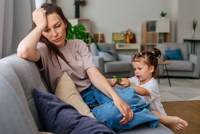 Tired woman sitting on couch while young daughter tries to get her attention, capturing cycle trip over watching daughter theme. Tired woman sitting on couch while young daughter tries to get her attention, capturing cycle trip over watching daughter theme.