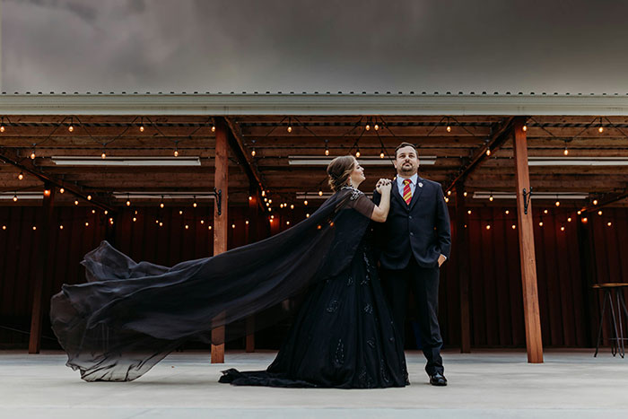 Bride in flowing black dress and fiancé in suit pose under string lights, reflecting tension with fiancé’s female friend demands. Bride in flowing black dress and fiancé in suit pose under string lights, reflecting tension with fiancé’s female friend demands.