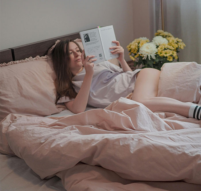 Woman reading a book while lying in bed with beige sheets and body positive plus-size theme implied by context Woman reading a book while lying in bed with beige sheets and body positive plus-size theme implied by context