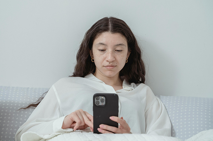 Young woman using smartphone while sitting on bed, reflecting body positive and plus-size awareness themes. Young woman using smartphone while sitting on bed, reflecting body positive and plus-size awareness themes.