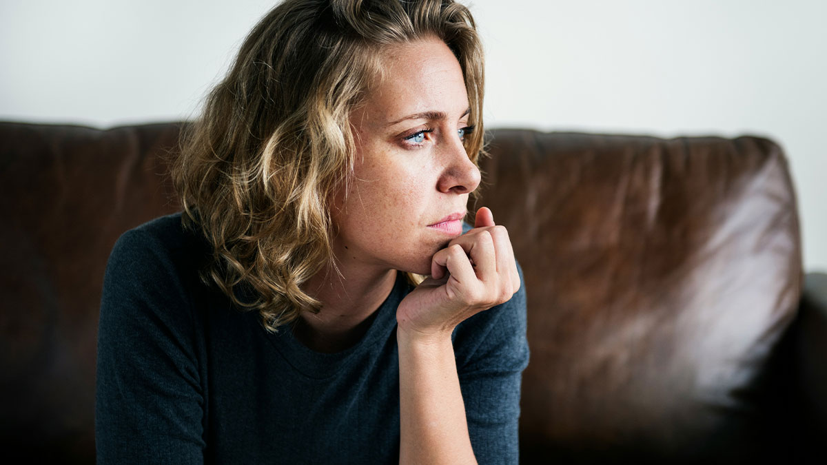 Woman with blonde hair sitting on a couch, looking thoughtful and concerned, illustrating bride resort room cancellation conflict.