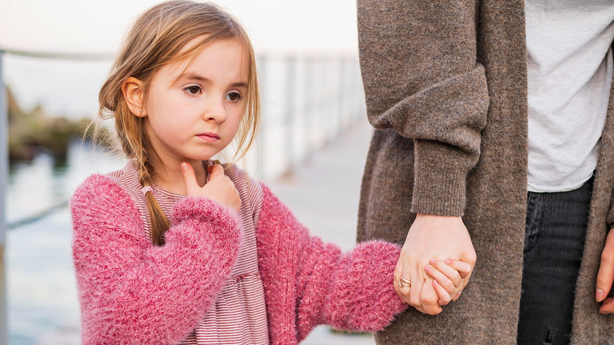 Young girl holding adult's hand looking worried, illustrating man might get divorced over secret kid revelation.