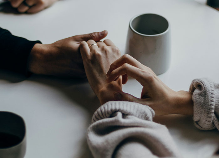 Two people holding hands over a table with cups, conveying honest emotions men never tell women about being stupid and ugly.