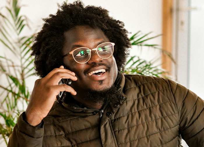 Smiling man with curly hair and glasses talking on phone, representing men getting brutally honest and sharing thoughts.