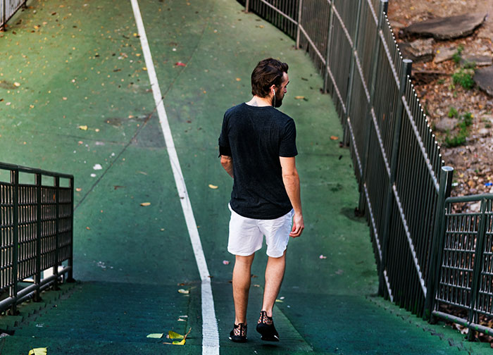Man wearing black shirt and white shorts walking down a green path, reflecting on what men never tell women about being stupid and ugly