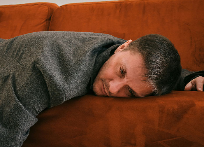 Man lying face down on a brown couch looking contemplative, reflecting the theme of men being brutally honest.