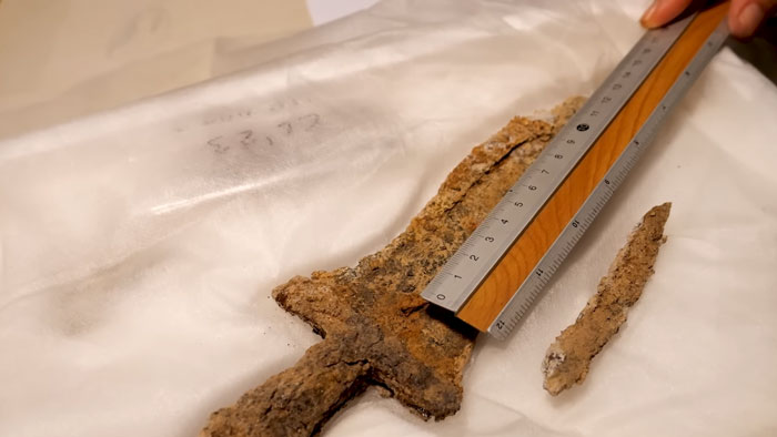 Ancient rusted sword being measured with a ruler, discovered during digging for solar farm construction site. Ancient rusted sword being measured with a ruler, discovered during digging for solar farm construction site.
