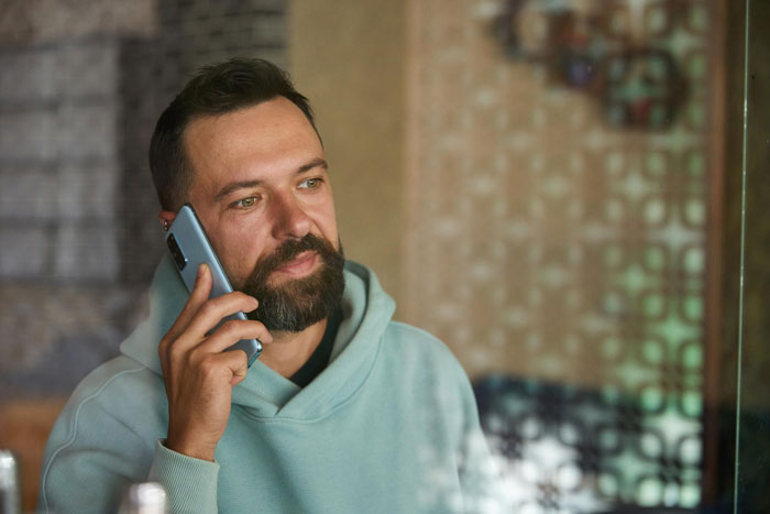 Man with beard making a phone call indoors, reflecting concern about neighbor meltdown after calling cops on 2YO wandering alone Man with beard making a phone call indoors, reflecting concern about neighbor meltdown after calling cops on 2YO wandering alone