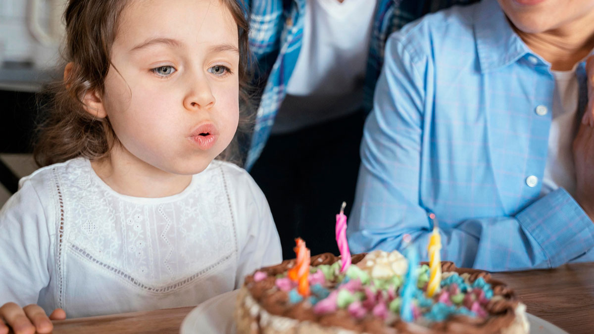 Young girl blowing out candles on birthday cake during party, illustrating family drama over cake payment dispute.