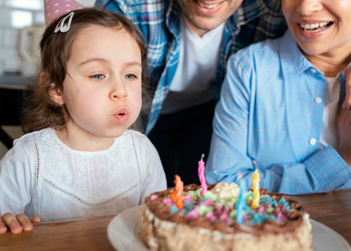 Young girl blowing out candles on a colorful birthday cake while family members smile nearby at a party. Young girl blowing out candles on a colorful birthday cake while family members smile nearby at a party.